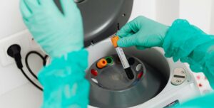 Gloved hands placing a blood sample tube into a laboratory centrifuge