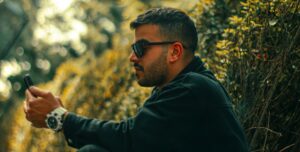A man in sunglasses sitting outdoors, looking at his phone
