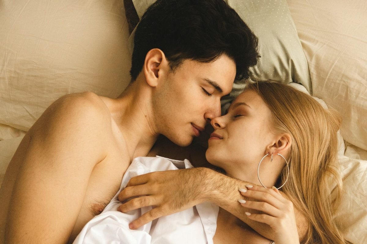Una pareja joven abrazada en la cama con las caras muy juntas