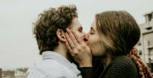 Pareja joven que se besa al aire libre, con las manos de ella en la cara de él