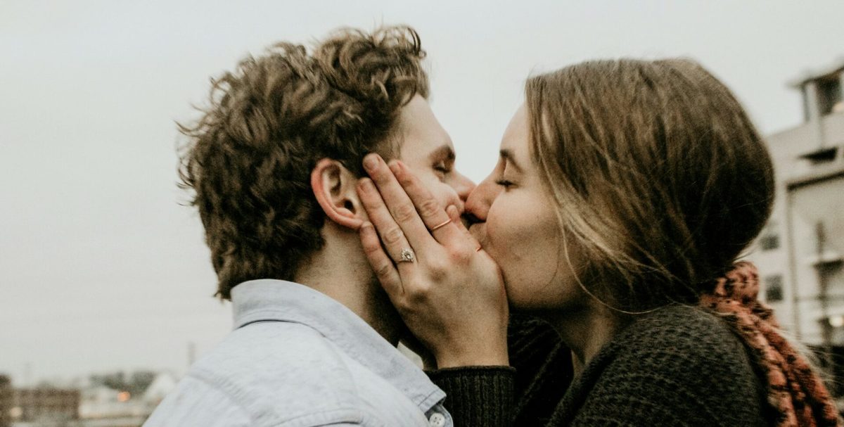 Pareja joven que se besa al aire libre, con las manos de ella en la cara de él
