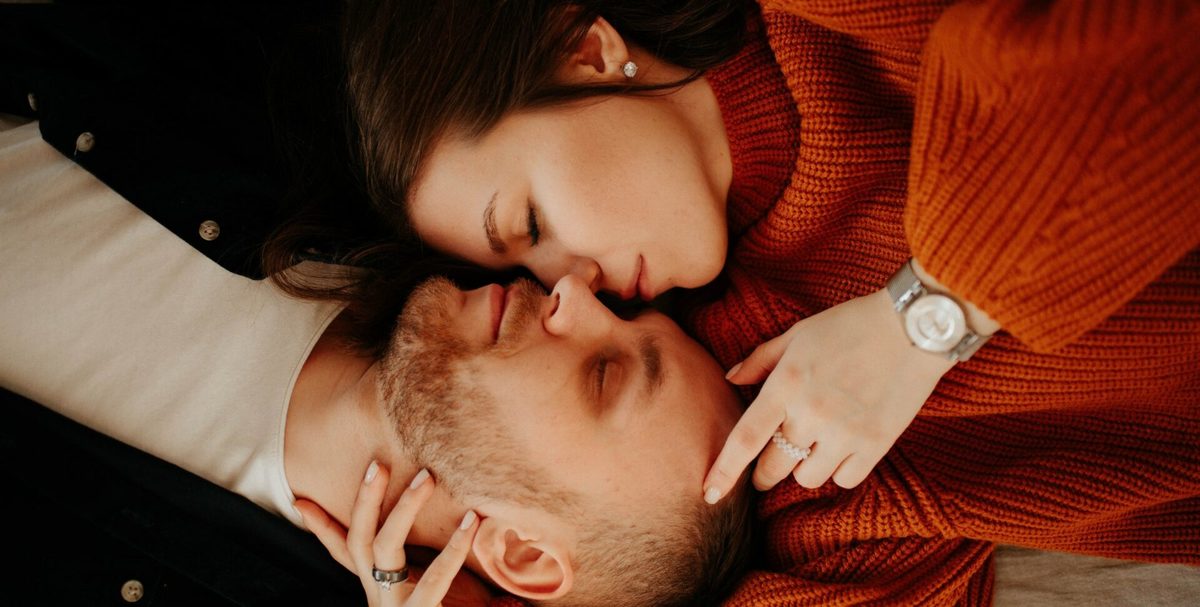 Pareja tumbada con las caras juntas, ella con un jersey naranja