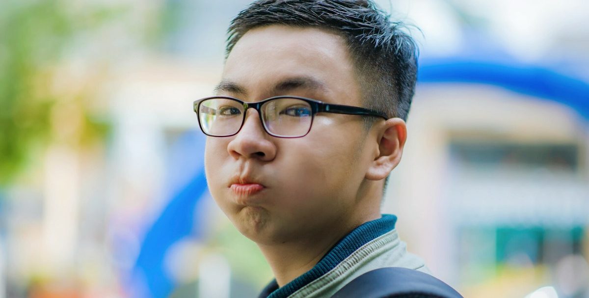 Joven con gafas inflando las mejillas, con un fondo desenfocado de colores