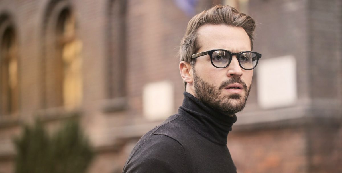 Un hombre con barba, gafas y jersey negro de cuello alto mira a un lado