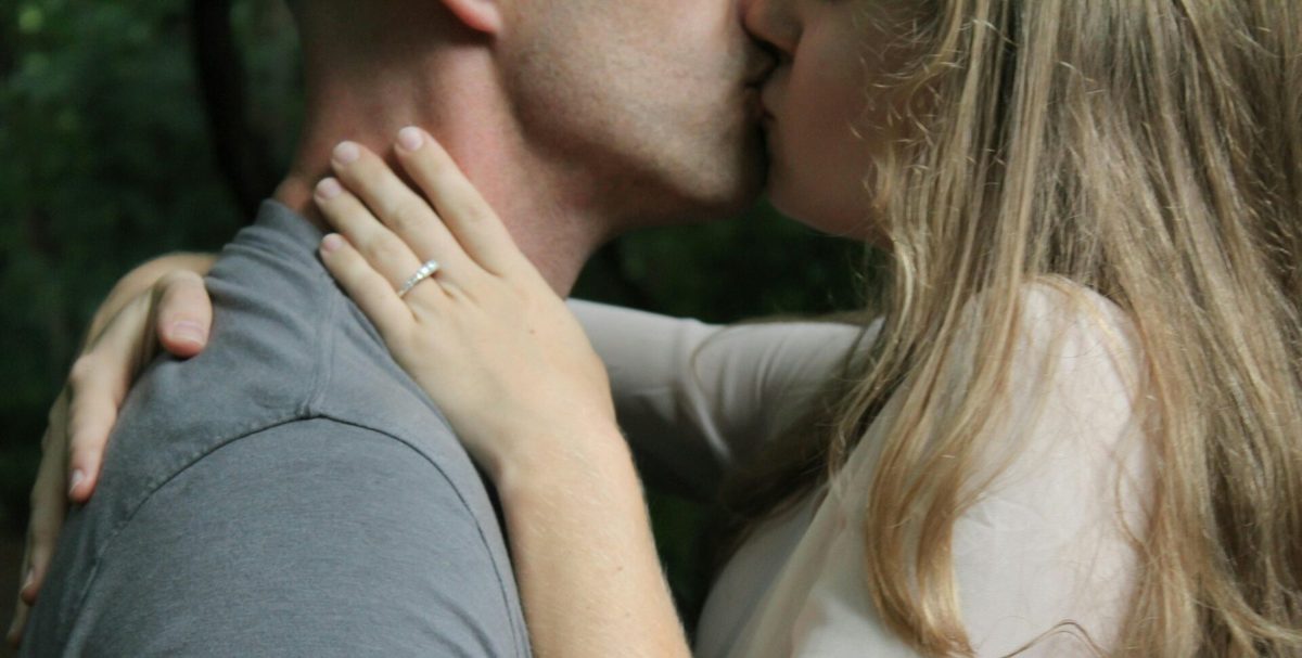 Una pareja se besa y ella apoya la mano en el hombro de él