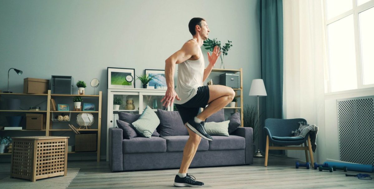 Hombre haciendo ejercicio en el salón de su casa, levantando la rodilla mientras corre en el sitio
