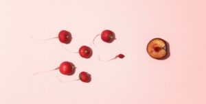 Rábanos colocados como espermatozoides que nadan hacia media ciruela sobre un fondo rosa
