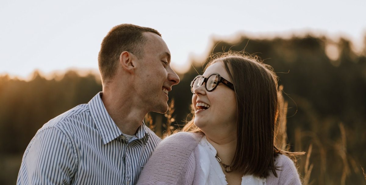 Pareja sonriendo y mirándose al aire libre al atardecer